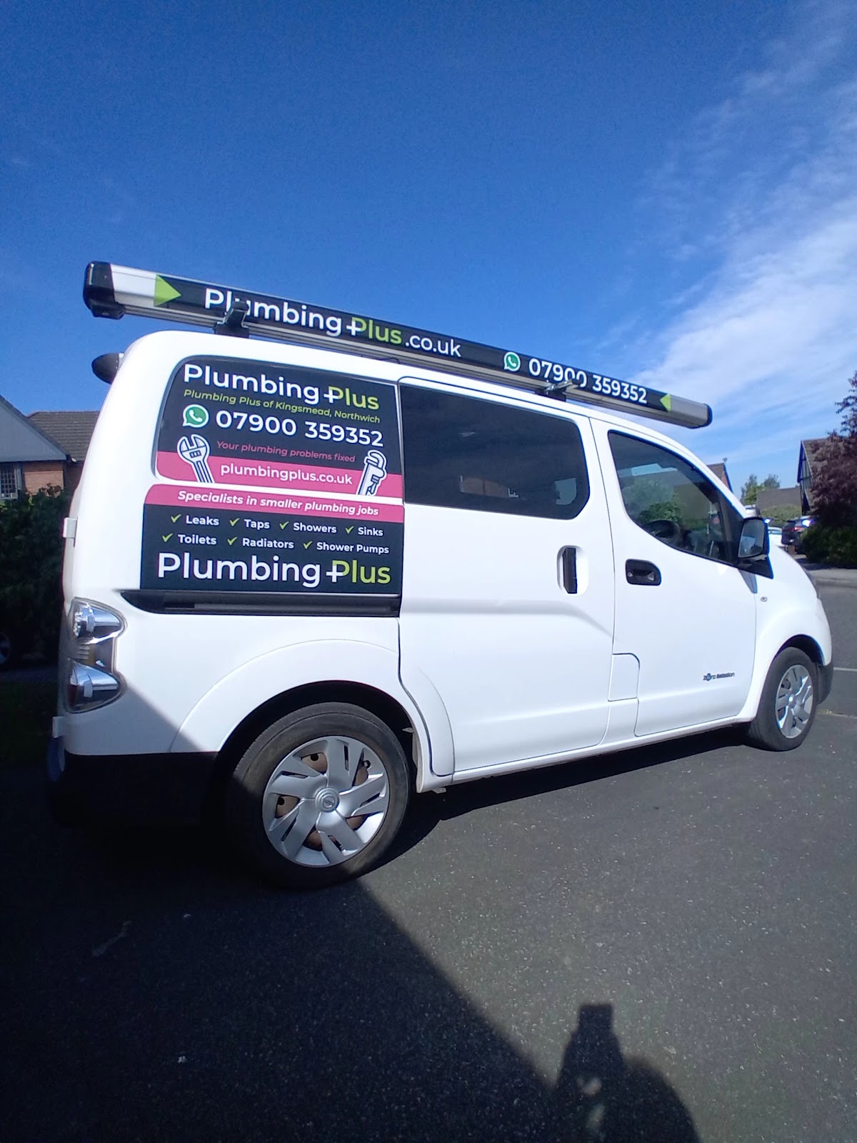 White Plumbing Plus branded van parked on residential street sunny day